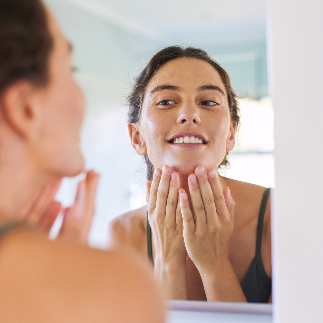 woman looking in mirror at glowing skin